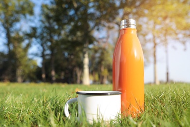 Photo of Modern orange thermos bottle and cup on green grass outdoors. Space for text