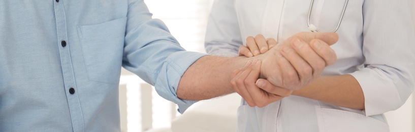 Image of Doctor checking pulse of senior patient in office, closeup. Banner design