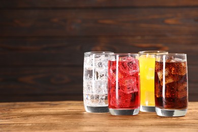 Photo of Glasses of different refreshing soda water with ice cubes on wooden table, space for text