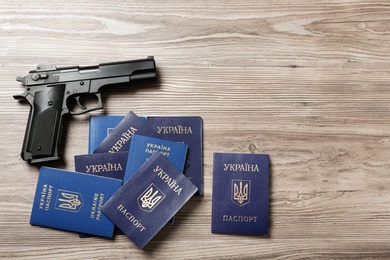 Photo of Gun with Ukrainian passports on wooden background, flat lay. Space for text