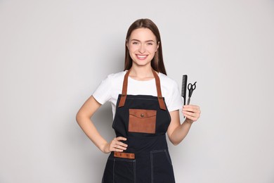 Photo of Portrait of happy hairdresser with comb and scissors on light background
