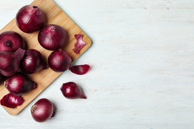 Photo of Board and red onions on white wooden table, flat lay. Space for text