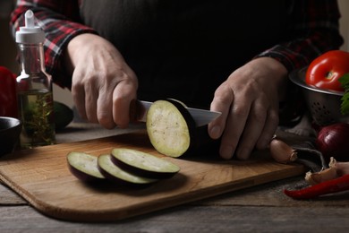 Photo of Cooking delicious ratatouille. Woman cutting fresh eggplant at wooden table, closeup