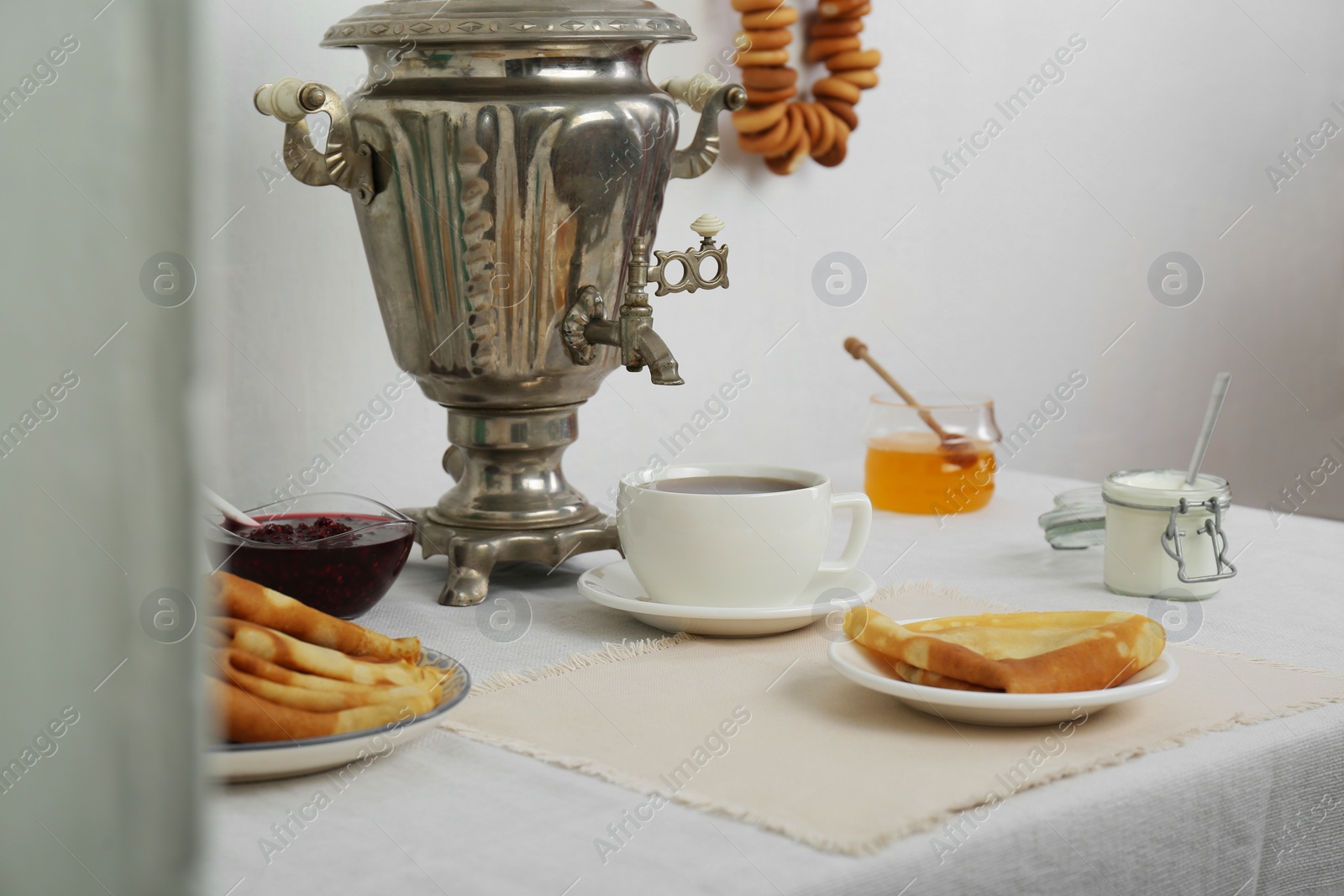 Photo of Vintage samovar, cup of hot drink and snacks served on table indoors. Traditional Russian tea ceremony