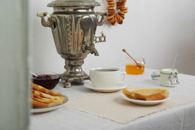 Photo of Vintage samovar, cup of hot drink and snacks served on table indoors. Traditional Russian tea ceremony