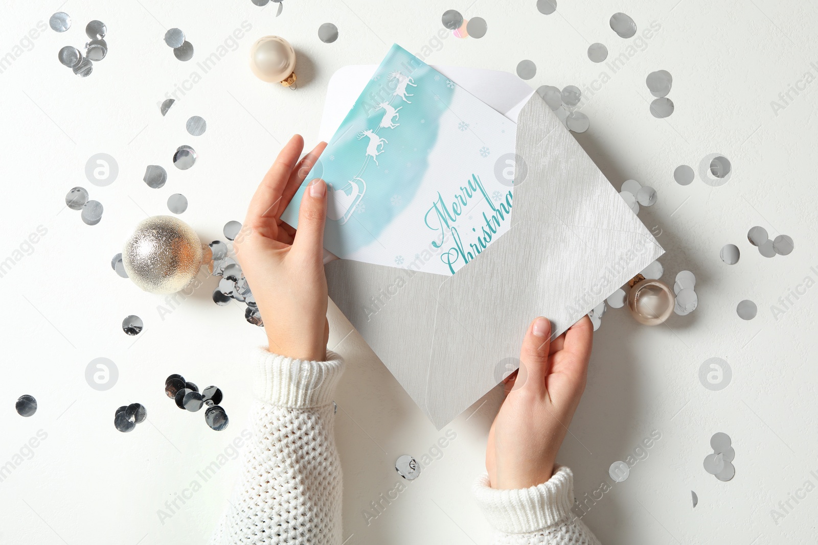 Image of Woman taking greeting card with text Merry Christmas from envelope at white table, top view