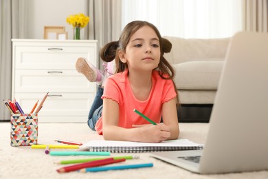Photo of Little girl drawing on paper with pencil at online lesson indoors. Distance learning