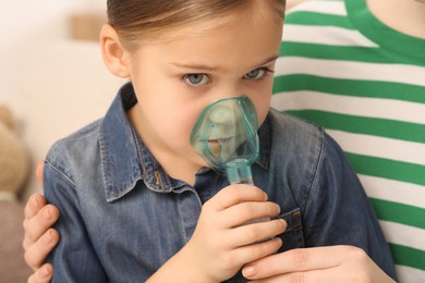 Photo of Mother helping her sick daughter with nebulizer inhalation at home