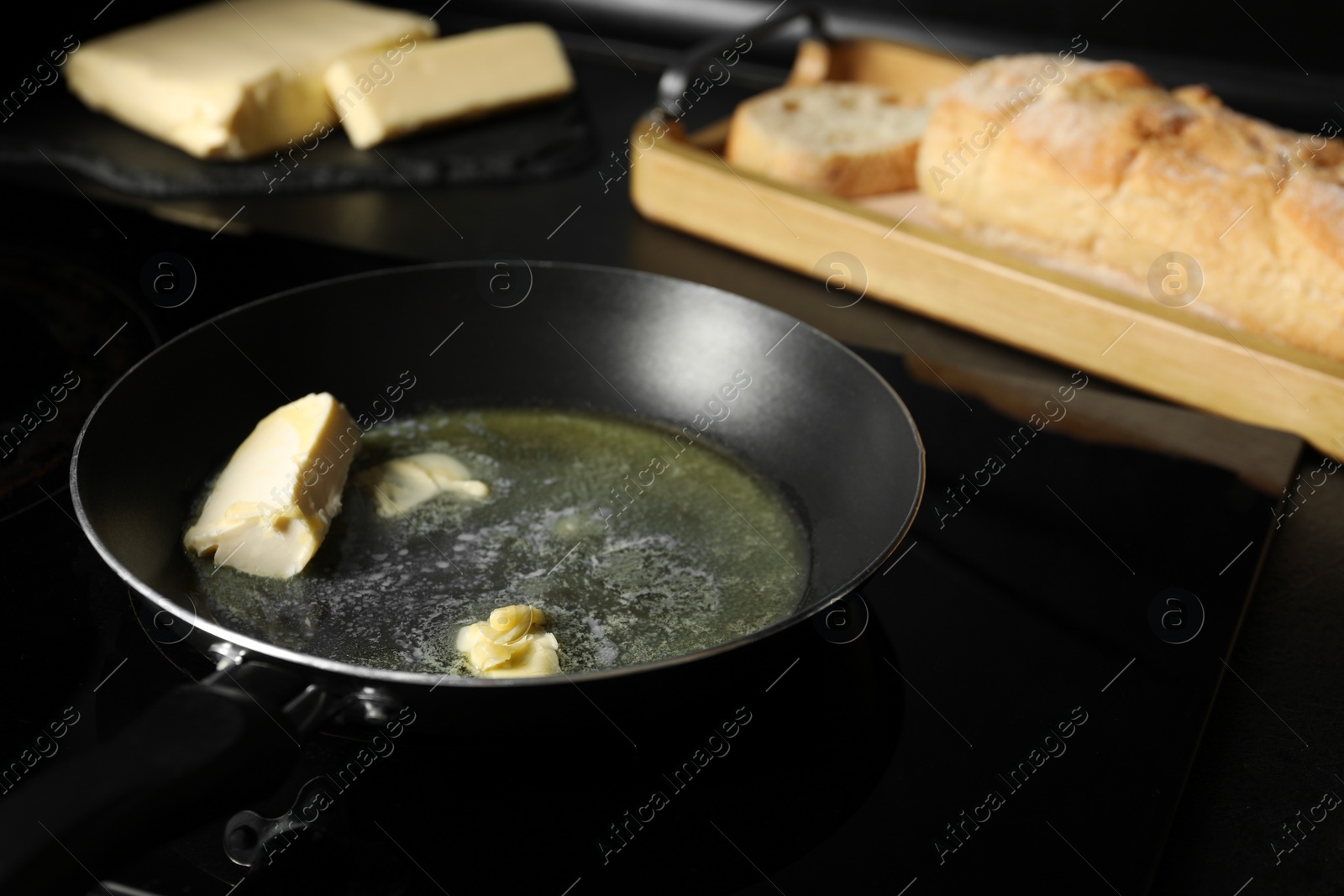 Photo of Melting butter in frying pan, dairy product and bread on black table