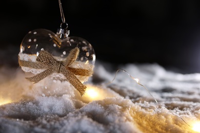 Photo of Glass heart and fairy lights on white snow outdoors. Space for text