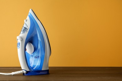 Photo of One modern iron on wooden table against orange background, space for text. Home appliance