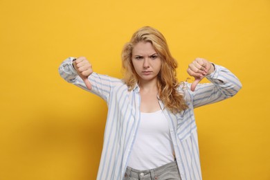 Photo of Dissatisfied young woman showing thumbs down on yellow background