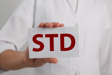 Photo of Doctor holding sheet of paper with abbreviation STD on white background, closeup