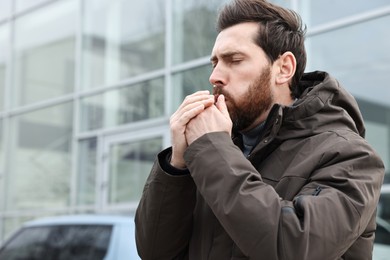 Photo of Sick man coughing on city street, space for text. Cold symptoms