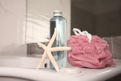 Photo of Pink sponge, starfish and shower gel bottle on washbasin in bathroom. Space for text