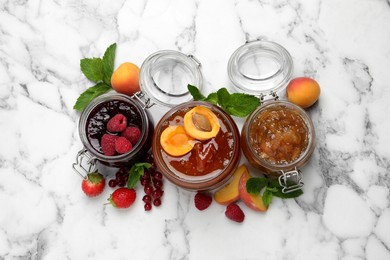 Photo of Jars with different jams and fresh fruits on white marble table, flat lay