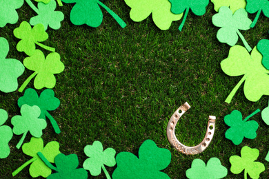 Photo of Frame made of clover leaves and horseshoe on grass, space for text. St. Patrick's Day celebration