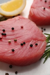 Photo of Raw tuna fillet with peppercorns, lemon and rosemary on white table, closeup