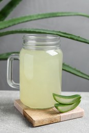 Photo of Tasty aloe juice in mason jar and cut fresh leaves on light grey table