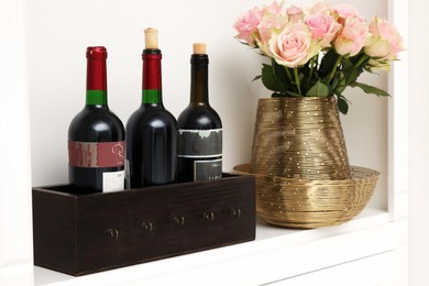 Photo of Shelf with different wine bottles and beautiful rose flowers indoors