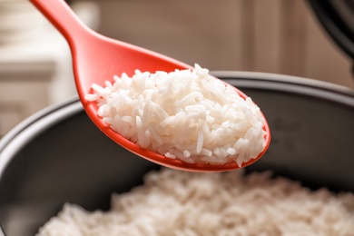 Photo of Spoon with tasty hot rice over cooker, closeup
