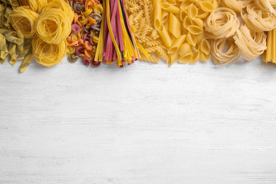 Photo of Different types of pasta on white wooden table, flat lay. Space for text