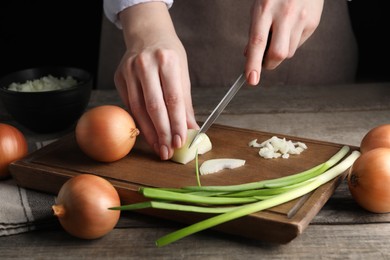 Woman cutting ripe onion at wooden table, closeup