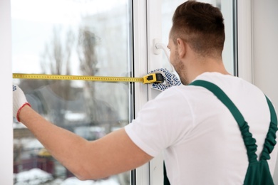 Photo of Construction worker measuring plastic window indoors. Professional installation