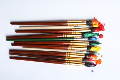 Photo of Brushes with colorful paints on white background, flat lay