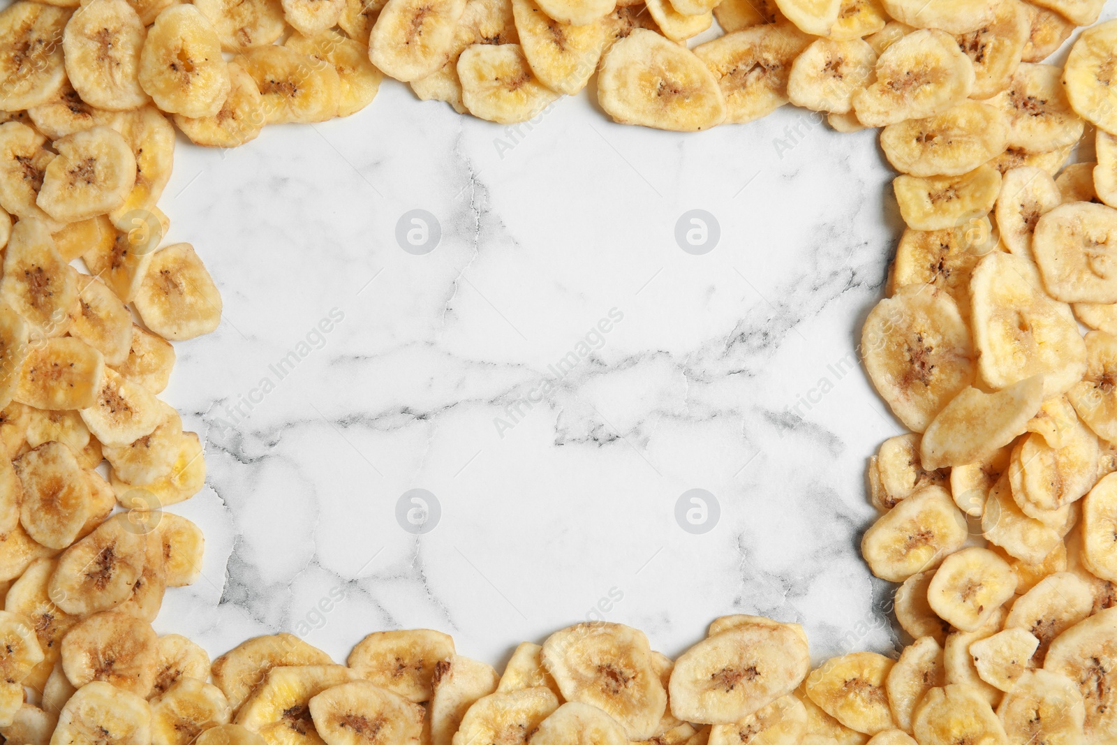 Photo of Frame made of sweet banana slices on marble background, top view with space for text. Dried fruit as healthy snack