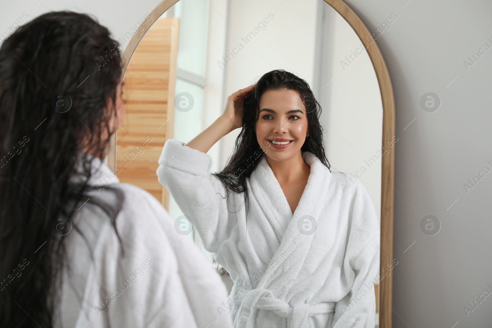 Photo of Beautiful young woman in bathrobe standing near mirror indoors