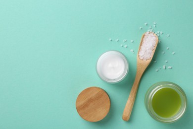 Photo of Moisturizing cream in open jars and sea salt on turquoise background, flat lay. Body care products