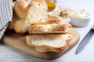 Photo of Cut freshly baked braided bread, knife and butter on white wooden table, closeup. Traditional Shabbat challah