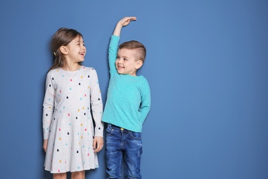 Photo of Little girl and boy measuring their height on color background