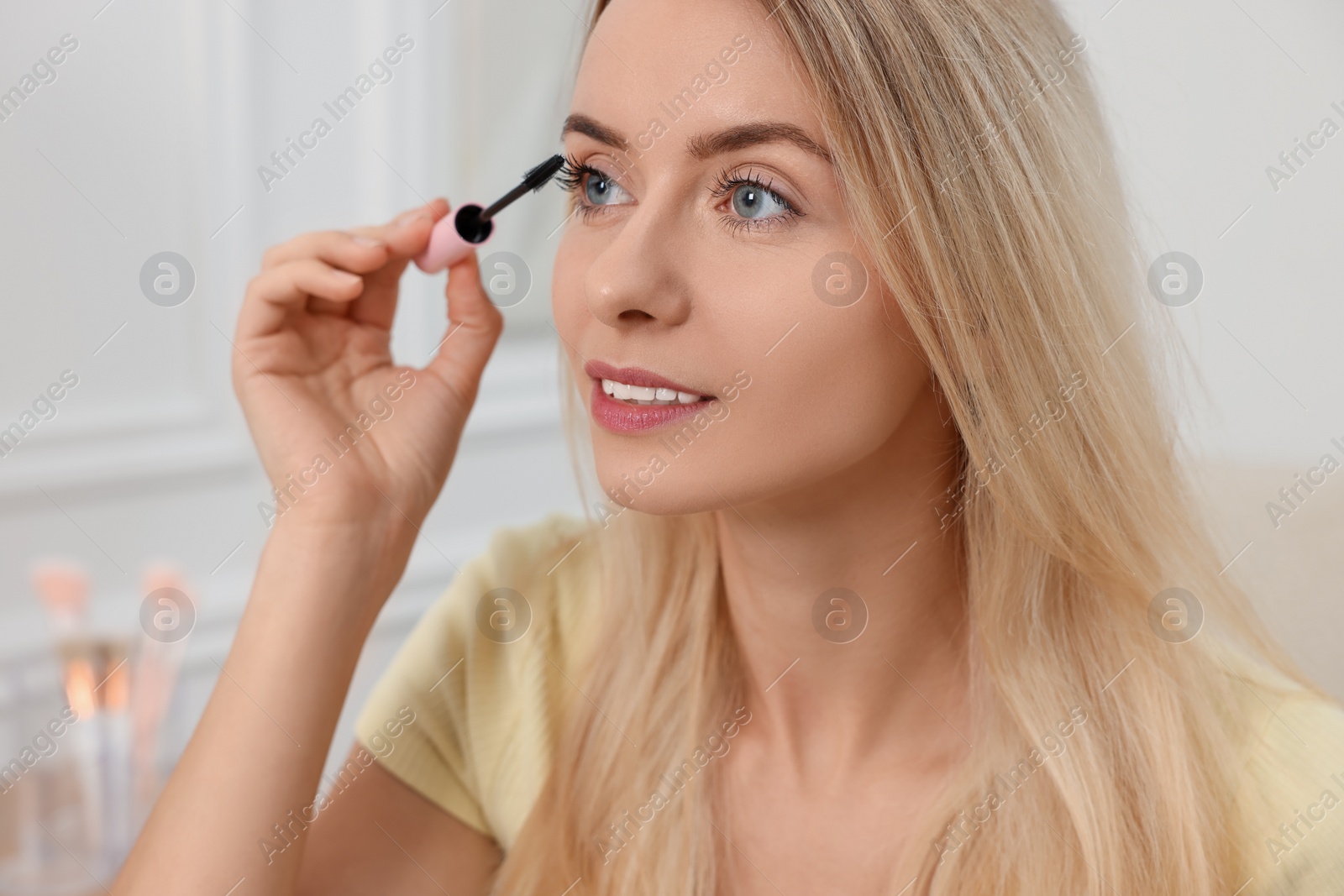 Photo of Beautiful woman applying mascara with brush indoors, closeup