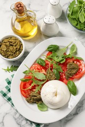 Photo of Delicious burrata salad with tomatoes, arugula and pesto sauce served on white marble table, flat lay