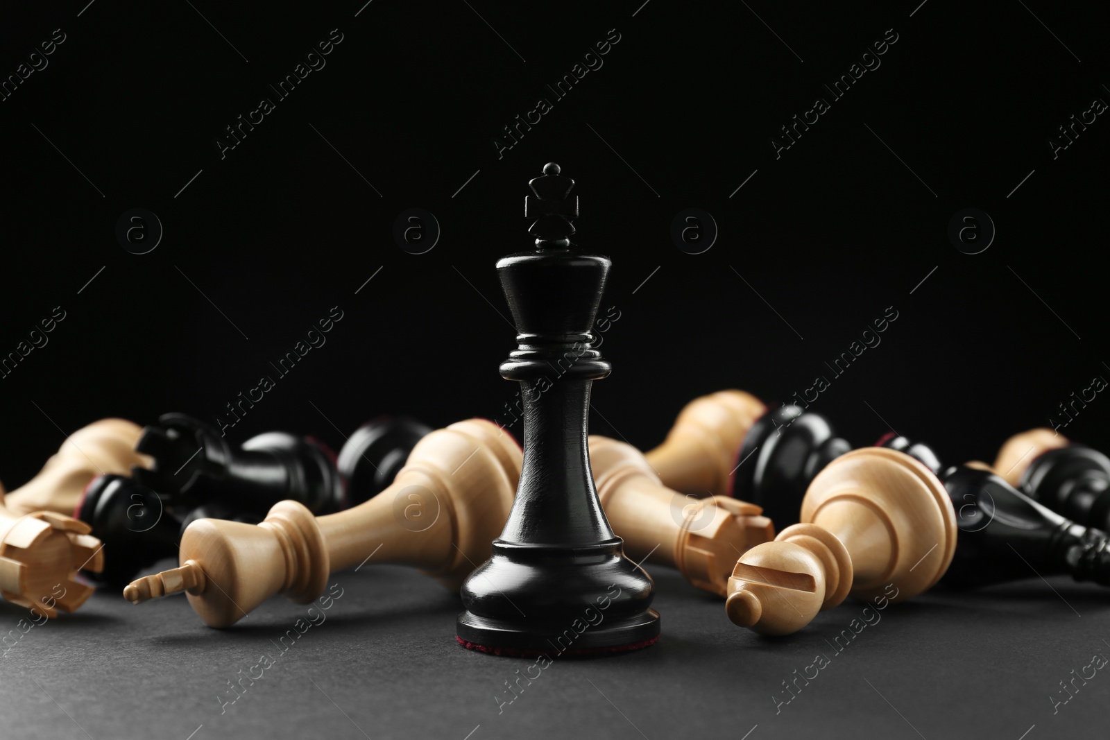 Photo of Black king among fallen chess pieces on dark background