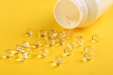 Photo of Vitamin capsules and medical bottle on yellow background, closeup