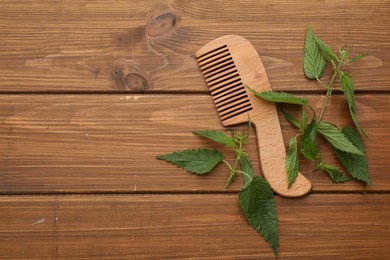 Photo of Stinging nettle and comb on wooden background, flat lay with space for text. Natural hair care