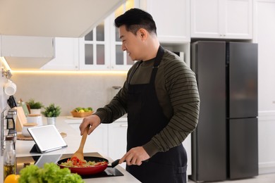 Photo of Man using tablet while cooking in kitchen