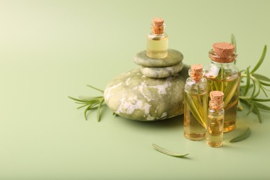 Photo of Aromatic essential oils in bottles, rosemary and pebble stones on green background. Space for text