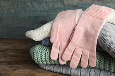 Photo of Stacked sweaters and gloves on wooden table, closeup. Autumn clothes