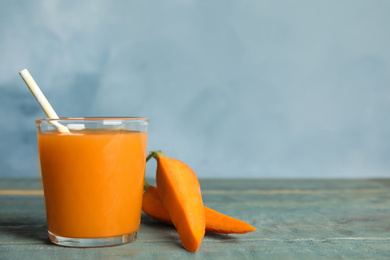 Photo of Freshly made carrot juice in glass on wooden table, space for text