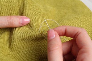 Photo of Woman with sewing needle and thread embroidering on cloth, closeup