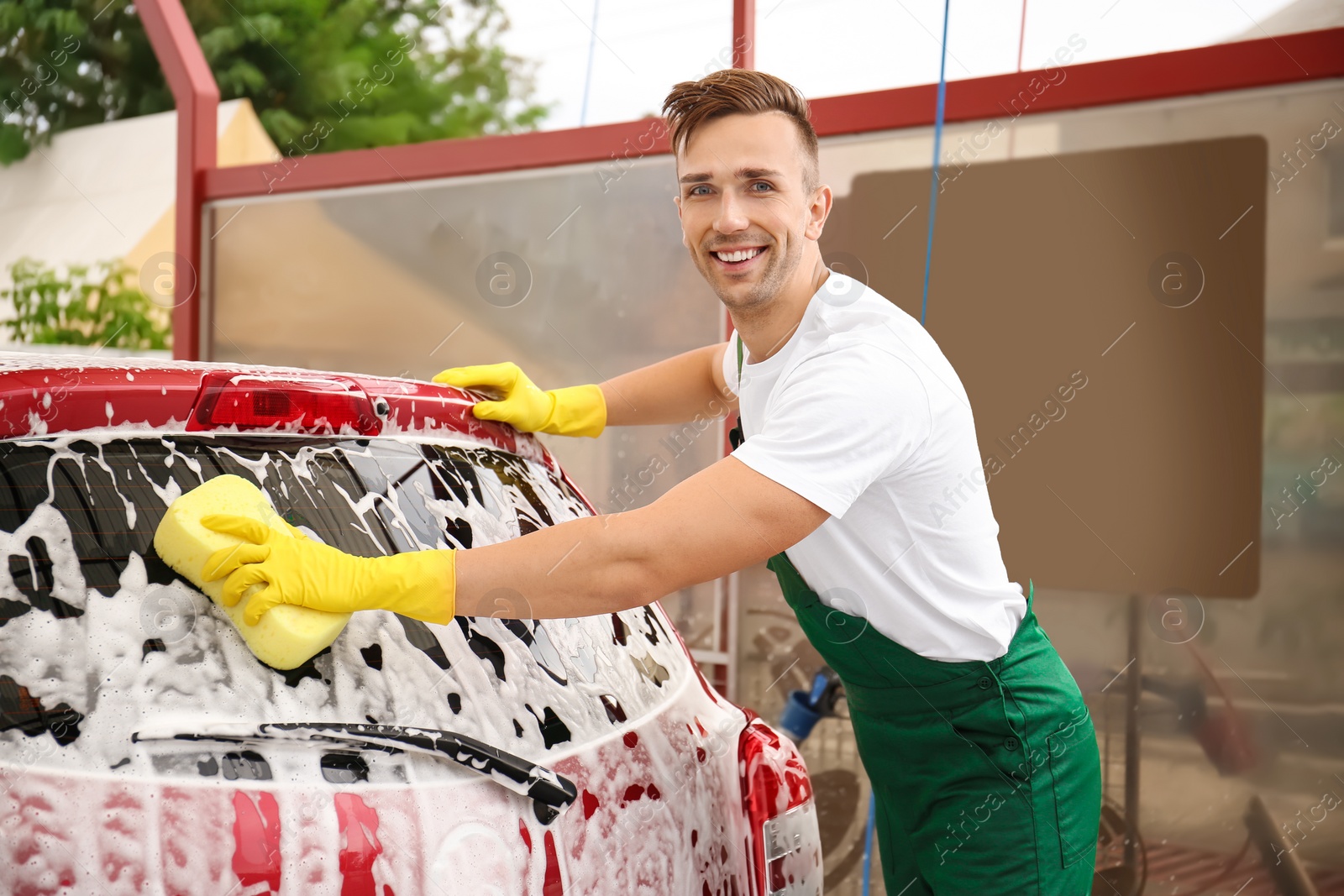 Photo of Male worker cleaning vehicle with sponge at car wash