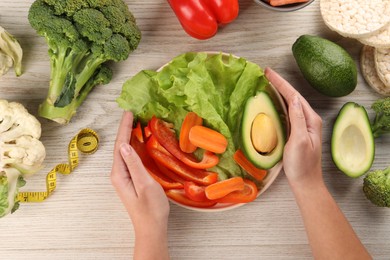 Photo of Healthy diet. Woman with fresh vegetables and measuring tape at light wooden table, top view
