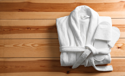 Photo of Clean folded bathrobe and slippers on wooden background, top view. Space for text