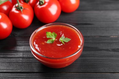 Photo of Delicious ketchup in bowl and tomatoes on black wooden table, closeup. Tomato sauce