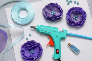 Photo of Hot glue gun, textile flowers and handicraft materials on color background, flat lay