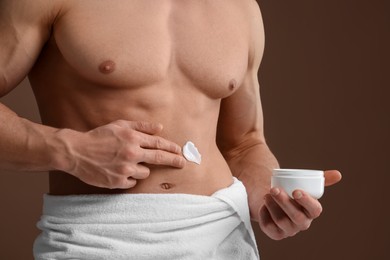 Photo of Man applying moisturizing cream onto his body on brown background, closeup